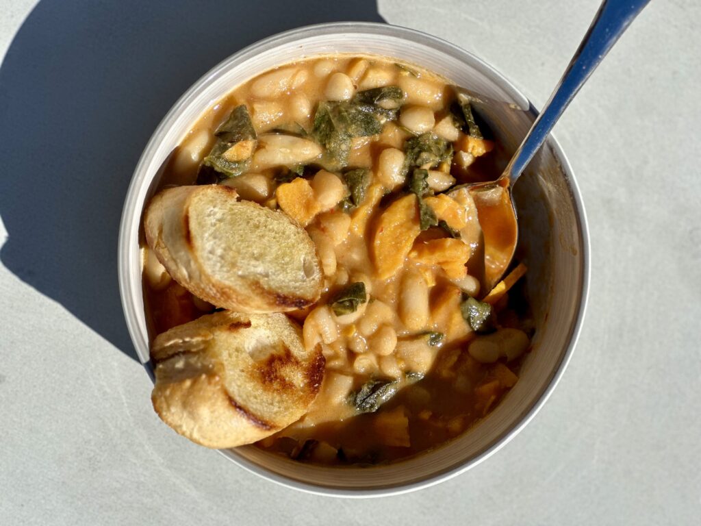 Image shows a bowl of Coconutty Beans & Greens Stew, the featured Blue Zone recipe on the blog.