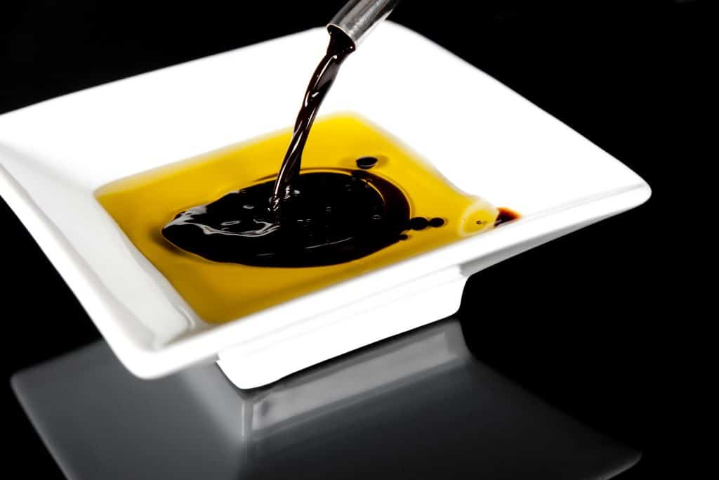 Rich balsamic vinegar and olive oil being poured onto a white plate, enhancing flavors in gourmet cooking. Perfect for salads, appetizers, or dipping bread in culinary dishes.