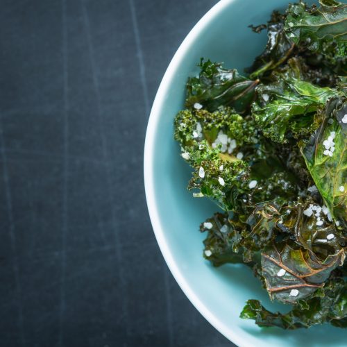 Fresh kale salad topped with coarse sea salt in a light blue bowl.
