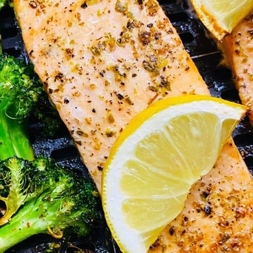 Succulent grilled salmon fillets seasoned with herbs served with fresh lemon wedges and grilled broccoli, perfect for healthy dining.