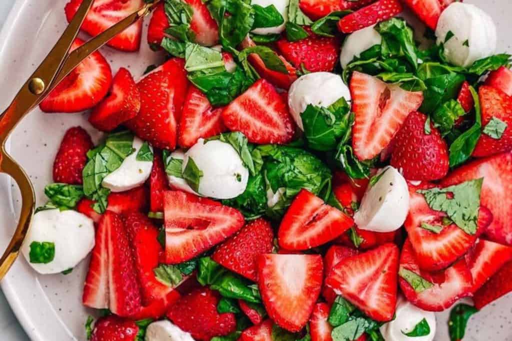 Fresh strawberry and basil salad with mozzarella cheese on a white platter, showcasing vibrant red strawberries, green basil leaves, and creamy mozzarella balls for a healthy and flavorful dish.