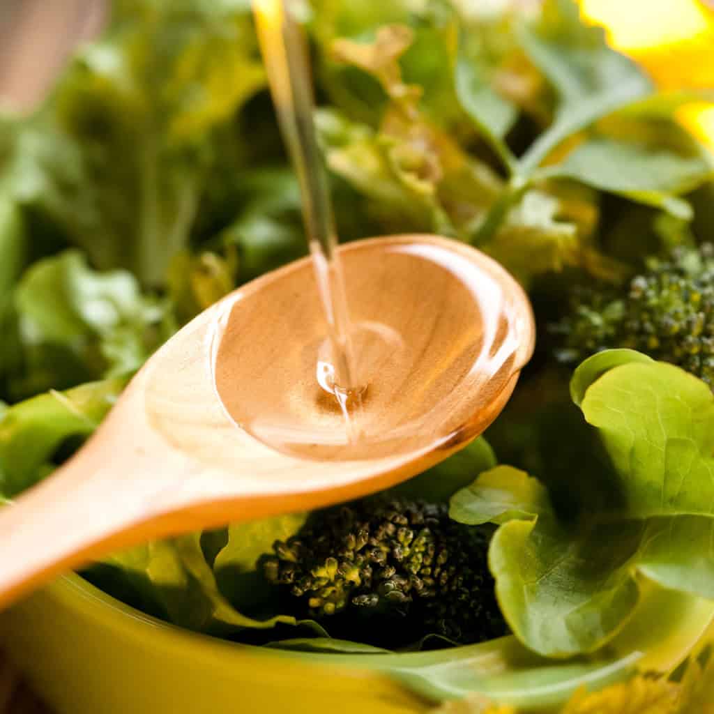 Pure spring water being poured into a wooden bowl surrounded by fresh green leafy vegetables, emphasizing healthy eating, natural foods, and hydration.