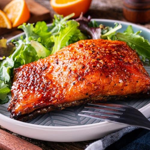 Juicy, grilled salmon fillet with crispy seasoned exterior served with fresh mixed greens on a rustic wooden table. Perfect for healthy seafood lovers and dinner recipes.