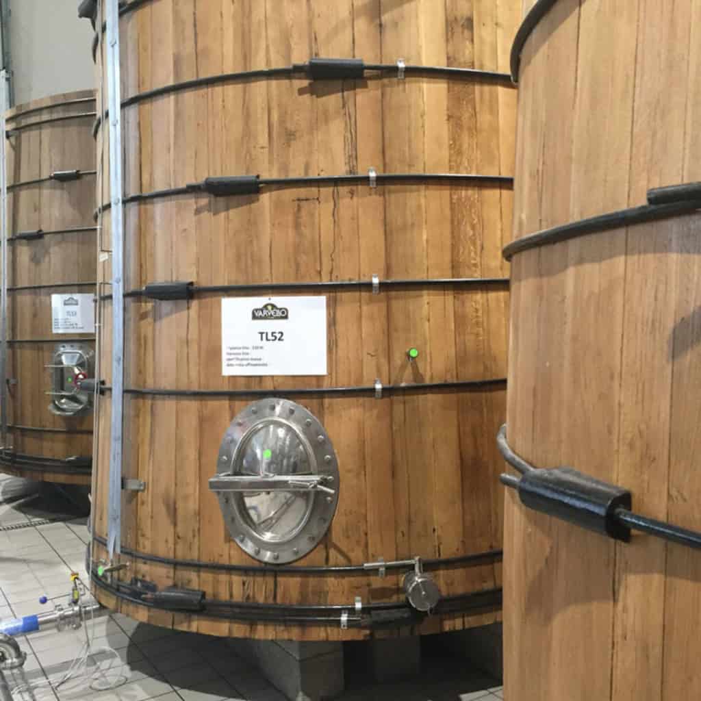 Stainless steel fermentation tank with wooden exterior, used for brewing beer or wine, equipped with pipes, valves, and control mechanisms for fermentation process.