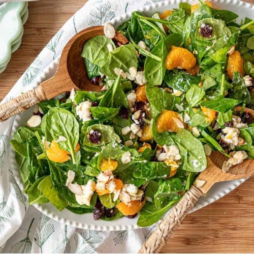 Fresh healthy salad featuring mixed greens, orange segments, feta cheese, and almonds, presented on a white platter. Ideal for nutritious dining, summer recipes, and farm-to-table cuisine.